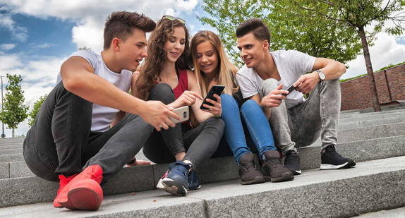 Vier Jugendliche sitzen auf einer Freitreppe und betrachten etwas auf dem Smartphone
