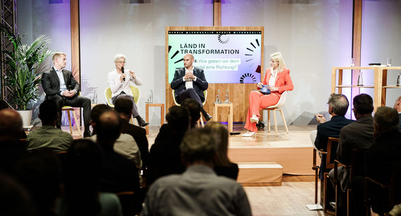 (v.l.n.r.) Dr. Stefan Hoops, CEO DWS KGaA, Dr. Brigitte Knopf, Direktorin Zukunft KlimaSozial und stv. Vorsitzende des Expertenrats für Klimafragen, Finanzminister Dr. Danyal Bayaz und Moderatorin Sonja Álvarez Sobreviela sitzen gemeinsam auf der Bühne. Im Vordergrund sieht man den vollen Saal.