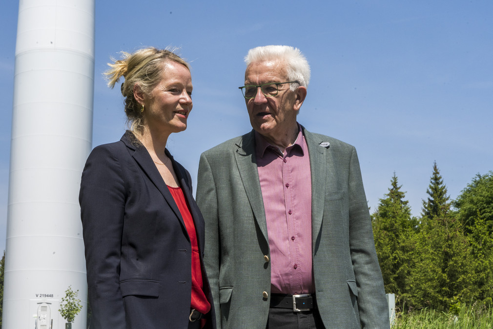 Ministerpräsident Winfried Kretschmann (rechts) und Umweltministerin Thekla Walker (links) stehen vor einem Windrad.