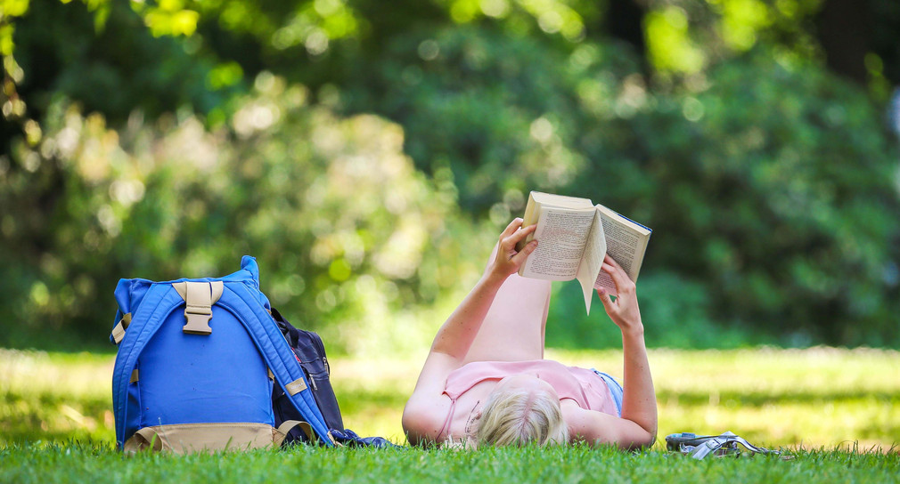 Symbolbild: Eine Studentin liegt bei schönem Wetter auf einer Wiese und liest ein Buch. (Bild: Mohssen Assanimoghaddam / dpa)