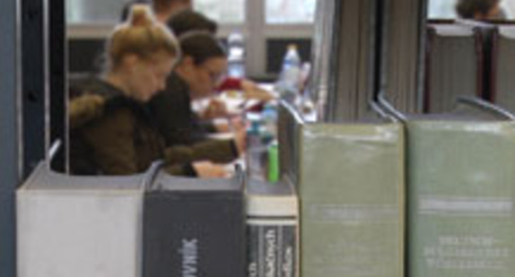 Studierende sitzen in einer Universitätsbibliothek und arbeiten.