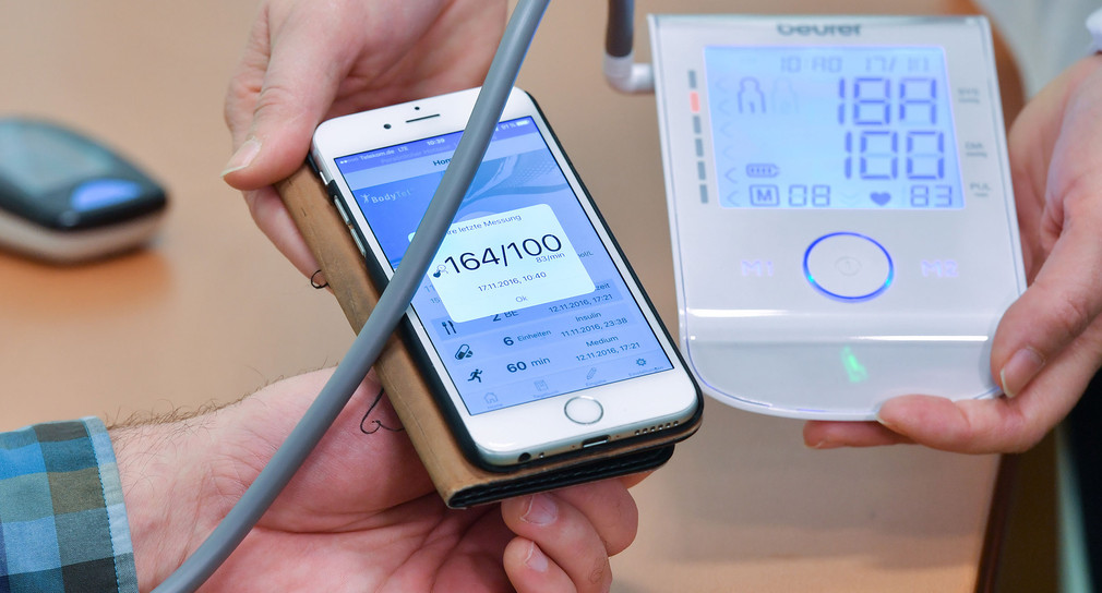 Eine Sozialarbeiterin misst die Blutdruckwerte eines Probanden und übermittelt diese drahtlos per Smartphone an einen Arzt.