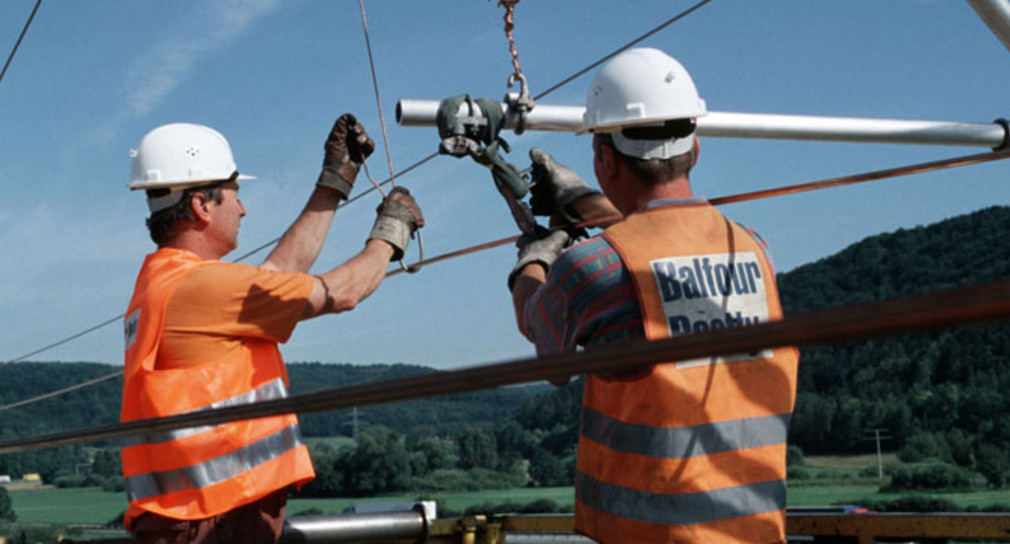 Zwei Arbeiter montieren den Fahrdraht einer Oberleitung (Bild: © Deutsche Bahn AG/Claus Weber).