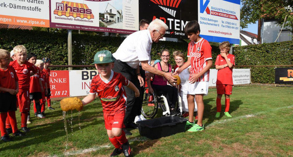 Ministerpräsident Winfried Kretschmann und Simone Fischer zusammen mit Kindern der inklusiven Ballschule beim Geschicklichkeitsspiel mit Wasser und Schwamm.