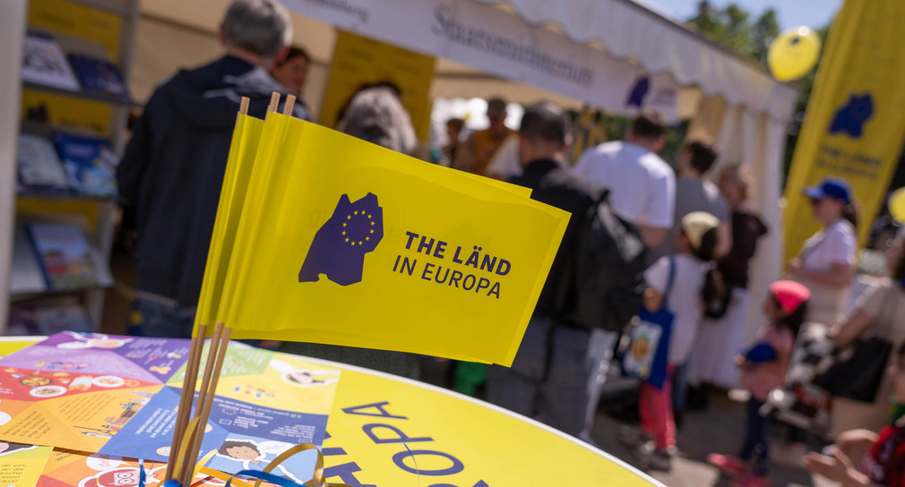 Kleine Fähnchen mit der Aufschrift „THE LÄND IN EUROPA“ stehen beim Europaaktionstag in Stuttgart auf einem Stehtisch.