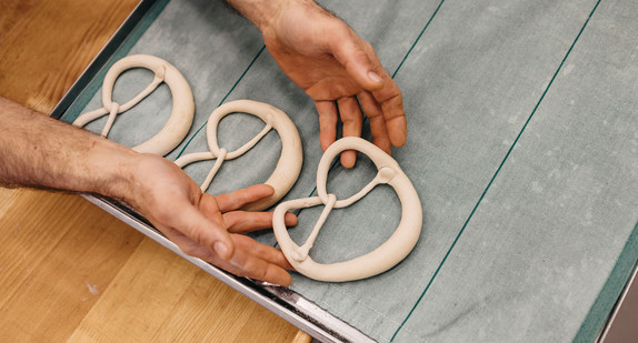 Ein Bäcker legt einen Brezel-Rohling auf das Backblech.