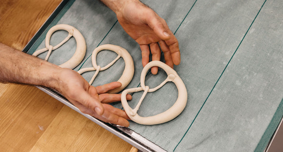 Ein Bäcker legt einen Brezel-Rohling auf das Backblech.