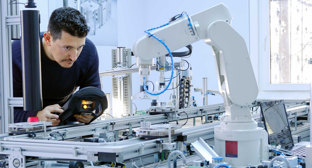 Ein Mann programmiert einen Roboterarm, der in einer Produktionslinie einer Smart Factory eingebaut ist.