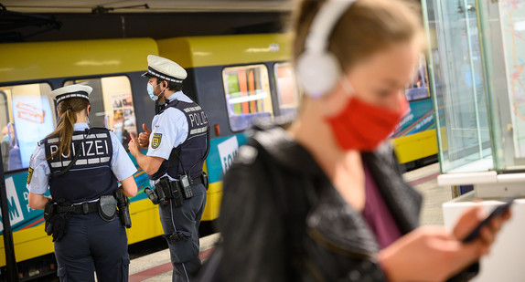 Polizeibeamte stehen an einer Haltestelle der Stuttgarter Straßenbahnen hinter einer Frau mit Mundschutz. (Bild: picture alliance/Sebastian Gollnow/dpa)