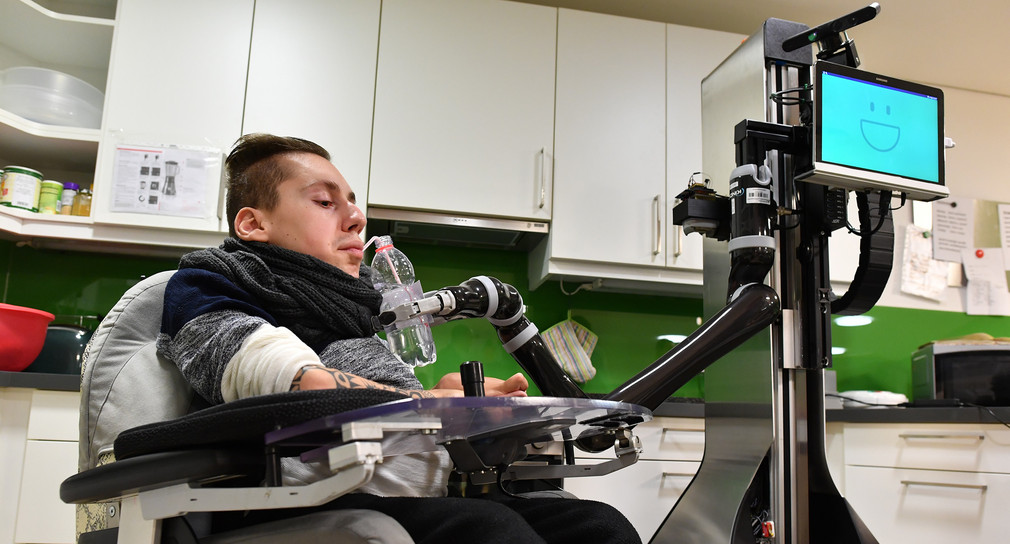 Rollstuhlfahrer Sascha Dohrn bedient im Körperbehindertenzentrum Oberschwaben in Weingarten mit einer Mundsteuerung den Roboter Marvin, der ihm eine Flasche Wasser reicht. (Bild: dpa)