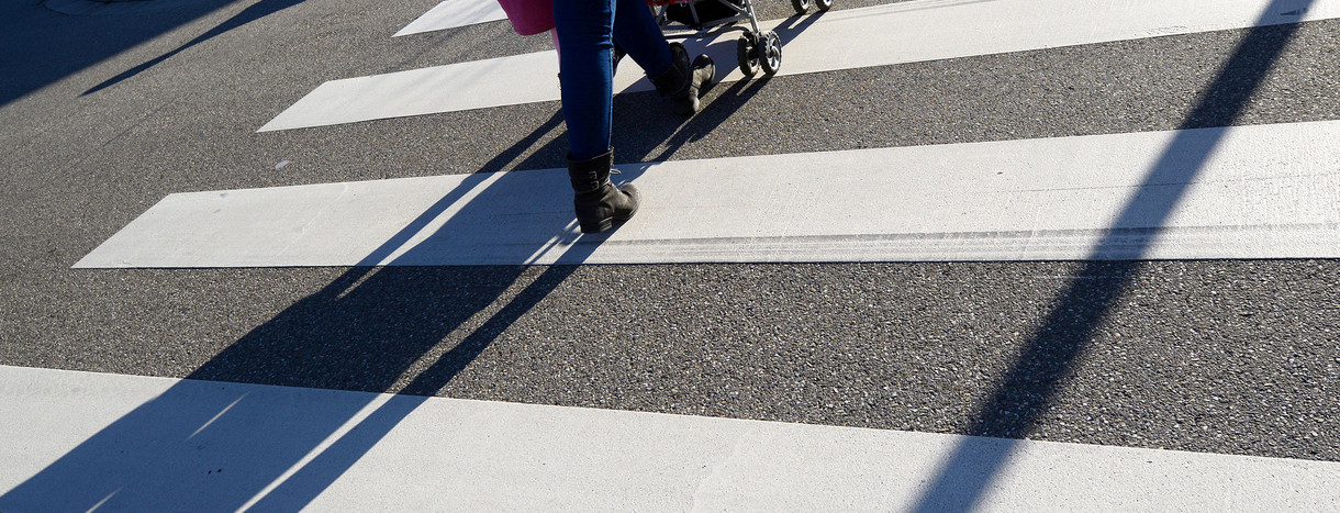 Eine Mutter geht mit einem Kinderwagen über einen Zebrastreifen.