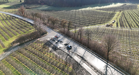 Ein frischer Radweg mit Bausstellenfahrzeugen, inmitten von landwirtschaftlicher Fläche. 
