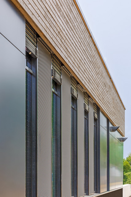 Blick entlang der westlichen Glasfassade mit Streckmetall verschatteten Fenster und Holzverschalung im oberen Bereich