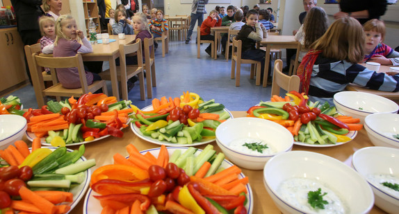 Schüler warten auf ihr Mittagessen, im Vordergrund stehen Teller mit geschnittenem Gemüse. (Foto: dpa)