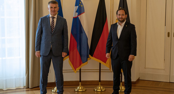 Staatssekretär Florian Hassler (r.) und der slowenische Botschafter Franc But (l.) stehen vor Fahnen.