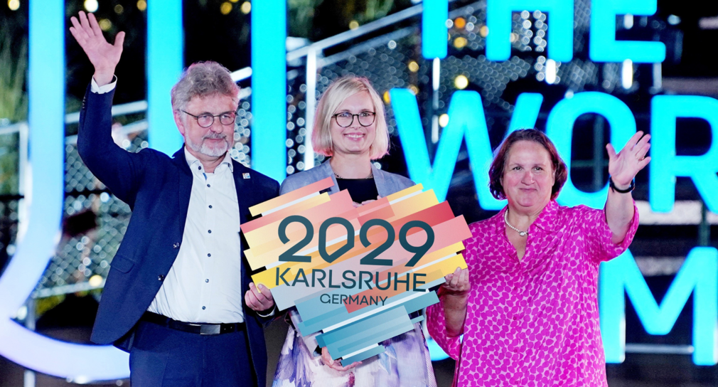 von links nach rechts: Dr. Frank Mentrup, Oberbürgermeister der Stadt Karlsruhe, Dr. Christiane Schenderlein, Staatsministerin für Sport und Ehrenamt in der Bundesregierung und Baden-Württembergs Sportministerin Theresa Schopper in Chengdu bei den World Games mit einem Herz in der Hand, das den Schriftzug Karlsruhe 2029 trägt.