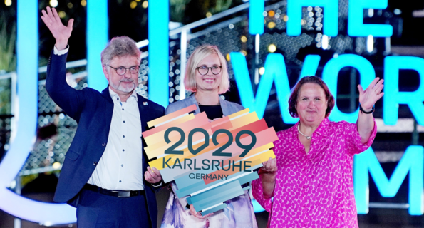 von links nach rechts: Dr. Frank Mentrup, Oberbürgermeister der Stadt Karlsruhe, Dr. Christiane Schenderlein, Staatsministerin für Sport und Ehrenamt in der Bundesregierung und Baden-Württembergs Sportministerin Theresa Schopper in Chengdu bei den World Games mit einem Herz in der Hand, das den Schriftzug Karlsruhe 2029 trägt.