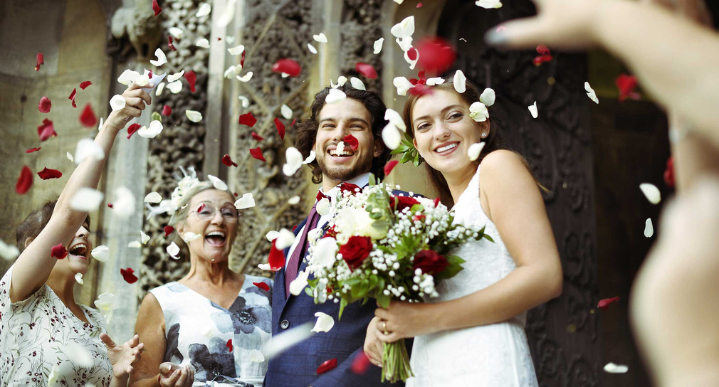 Ein Hochzeitspaar wird vor der Kirche mit Blütenblättern beworfen.