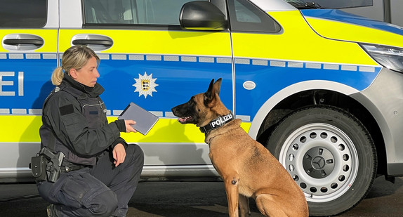 Polizistin mit Datenträgerspürhund vor Dienstwagen