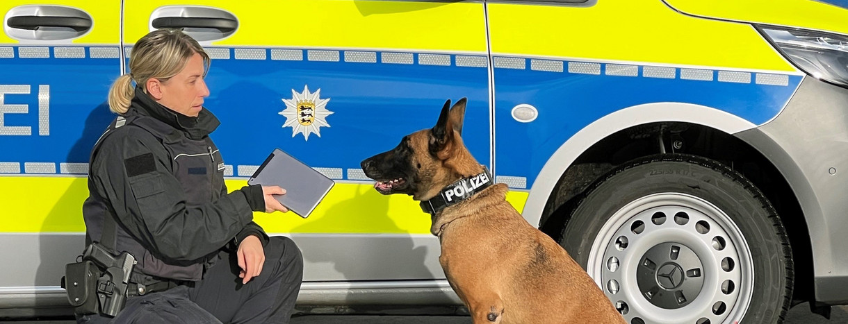 Polizistin mit Datenträgerspürhund vor Dienstwagen