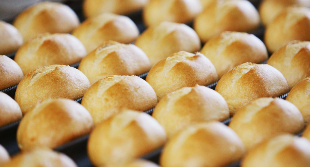 Symbolbild: Brötchen auf dem Fließband kommen aus dem Ofen. (Bild: Achim Scheidemann / dpa)