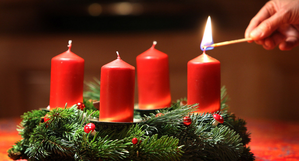 Eine Frau entzündet an einem selbst gebundenen Adventskranz eine Kerze. (Foto: © dpa)