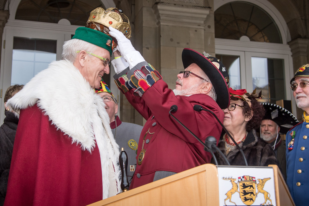 Narrenpräsident Roland Wehrle (M.) setzt Ministerpräsident Winfried Kretschmann (l.) eine Krone auf.