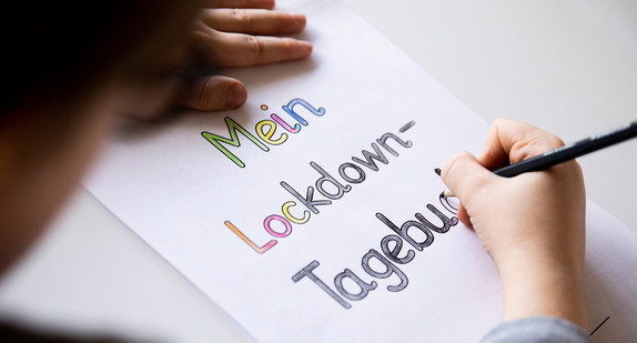 Ein Grundschüler malt an einem Tisch im Wohnzimmer die Buchstaben eines Lockdown Tagebuchs aus.
