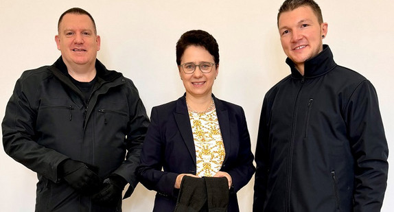 von links nach rechts: Thorsten Klay (Stellvertretender Landesvorsitzender und Geschäftsführer der Deutschen Justiz-Gewerkschaft Baden-Württemberg), Justizministerin Marion Gentges und Adrian Peschla (Stellvertretender Vorsitzender des Deutschen Gerichtsvollzieher Bunds Baden-Württemberg) mit Gegenständen der Schutzausrüstung