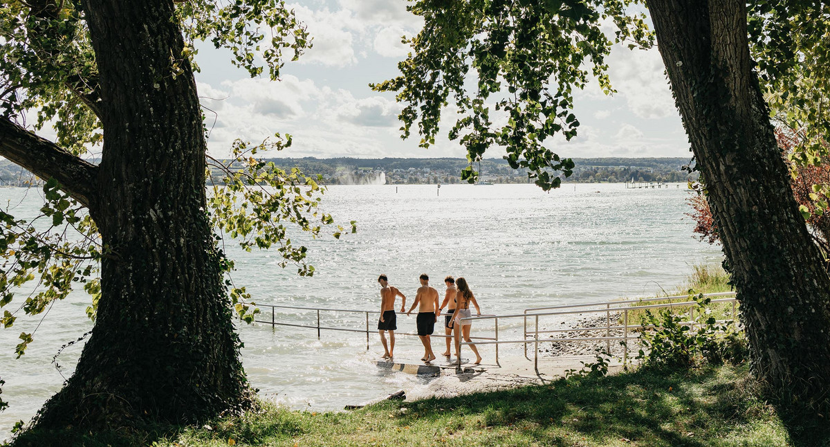 Eine Gruppe junger Menschen gehen ins Wasser, um im Bodensee zu schwimmen.
