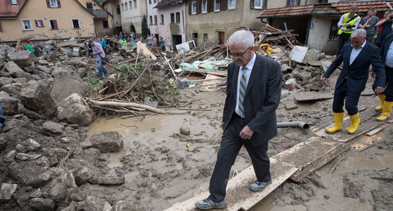 Ministerpräsident Winfried Kretschmann (l.) und Innenminister Thomas Strobl (r.) gehen in Braunsbach über Holzbretter. (Foto: dpa)