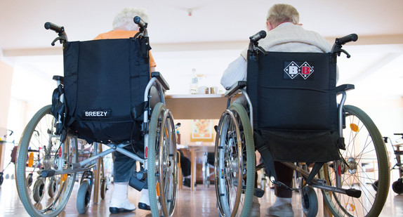 Zwei pflegebedürftige Frauen sitzen in einem Pflegeheim in ihren Rollstühlen nebeneinander. (Foto: © dpa)