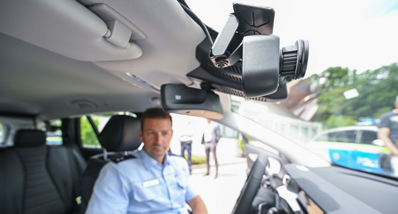 Ein Polizist sitzt in einem Polizeifahrzeug in dem ein Dashcam-System angebracht ist.