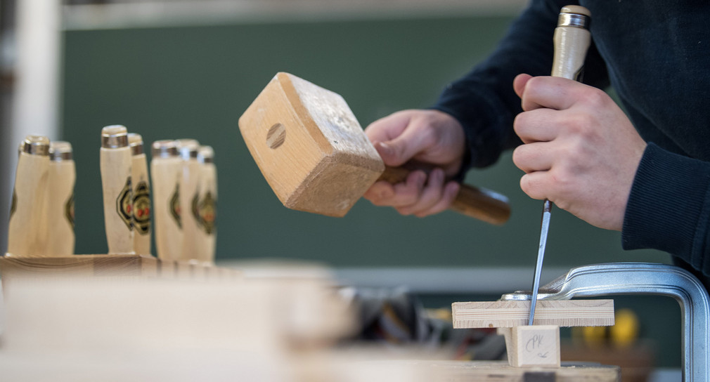 Ein Auszubildender im Handwerk arbeitet am an einer Berufsschule an einer Werkbank mit Holz.