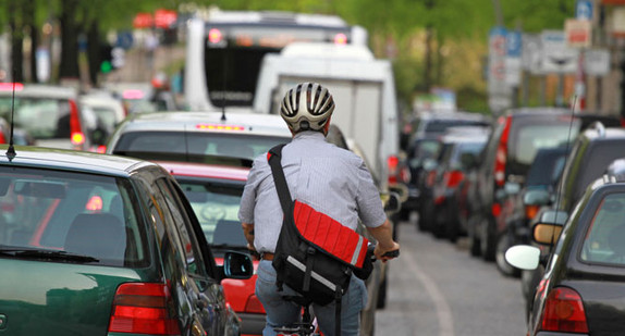 Fahrradfahrer mit Helm auf einer innenstädtischen Straße zwischen Autos (Bild: Fotolia, © Kara).