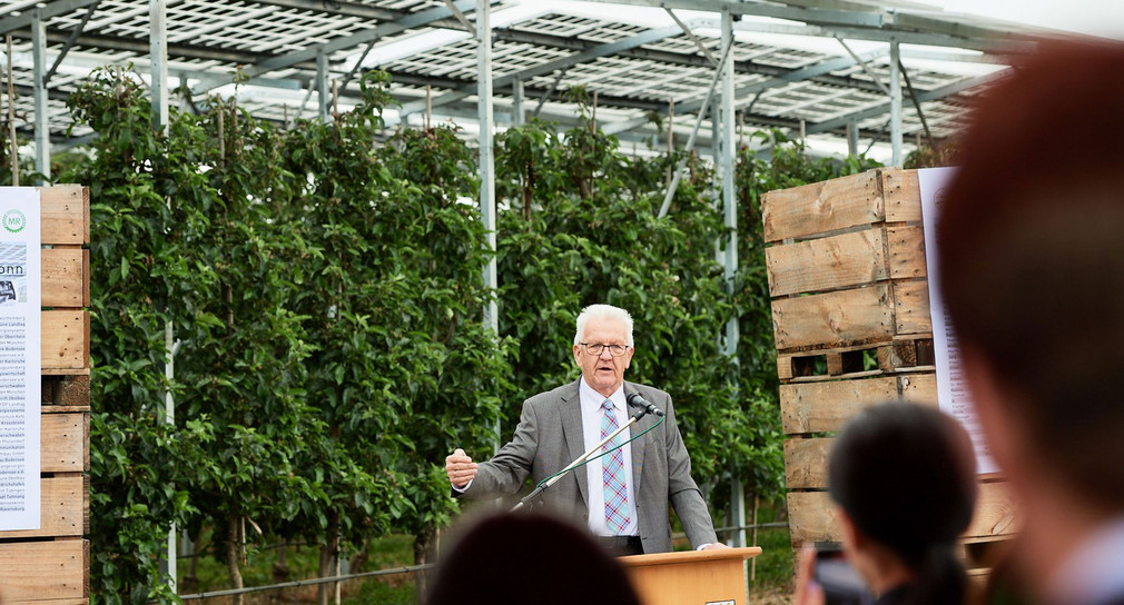 Ministerpräsident Winfried Kretschmann bei der Einweihung einer Photovoltaik-Anlage auf einem Feld mit Apfelbäumen in Kressbronn am Bodensee.