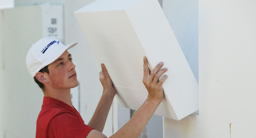 Ein Arbeiter montiert eine Styroporplatte zur Wärmedämmung an eine Fassade.