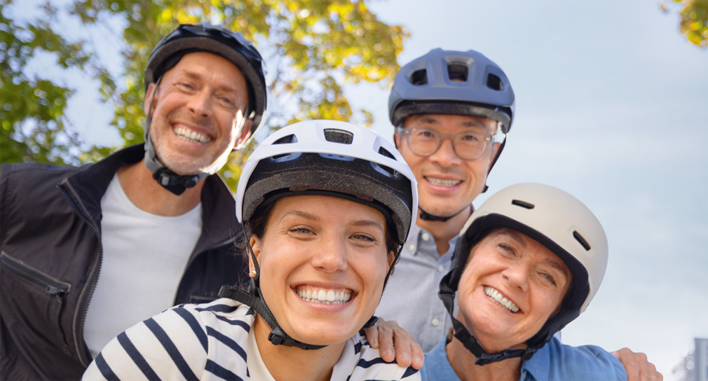 Vier Menschen stehen lächeld da und tragen Fahrradhelme.