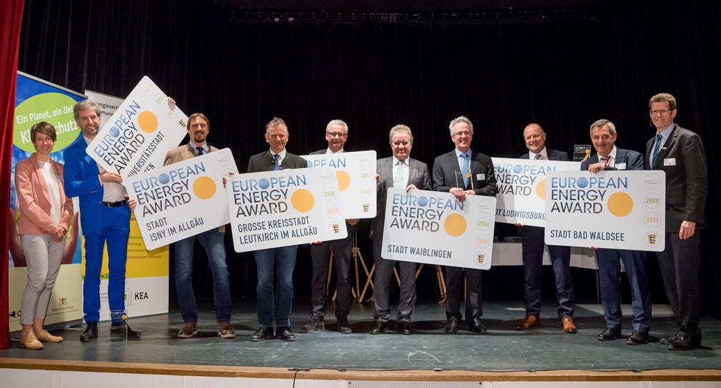 Charlotte Spörndli, Association European Energy Award AISBL (links), Umweltminister Franz Untersteller (Mitte) und Dr. Volker Kienzlen, Geschäftsführer der KEA Klimaschutz- und Energieagentur Baden-Württemberg (rechts) mit den sieben Gewinnern des European Energy Awards 2018, die mit „Gold“ ausgezeichnet wurden.