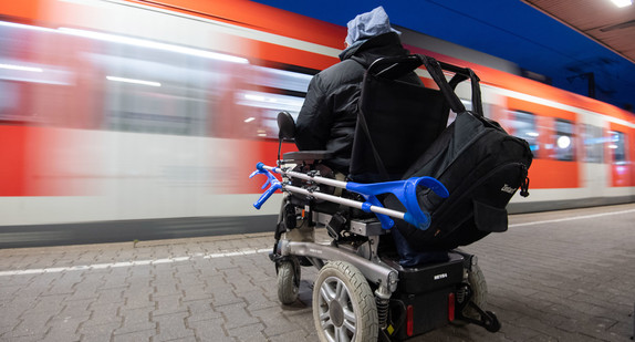 Ein Rollstuhlfahrer steht mit seinem Elektro-Rollstuhl am Bahnhof an einem Gleis. (Bild: picture alliance/Marijan Murat/dpa)