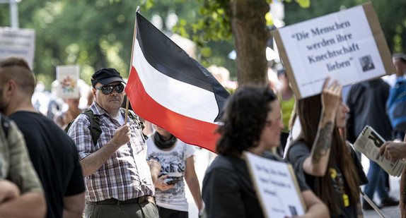 Ein Teilnehmer der Demonstration gegen die Corona-Beschränkungen trägt eine Flagge des Deutschen Reiches.