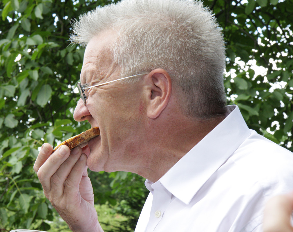 Ministerpräsident Winfried Kretschmann isst eine Scheibe Brot mit dem Regierungshonig