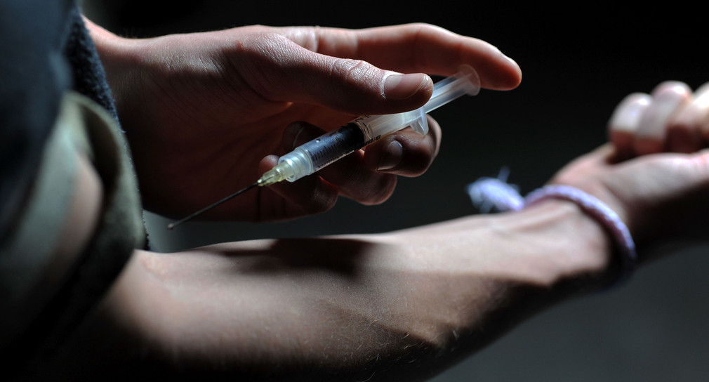 Ein Mann setzt sich eine Spritze mit Heroin in den Arm.