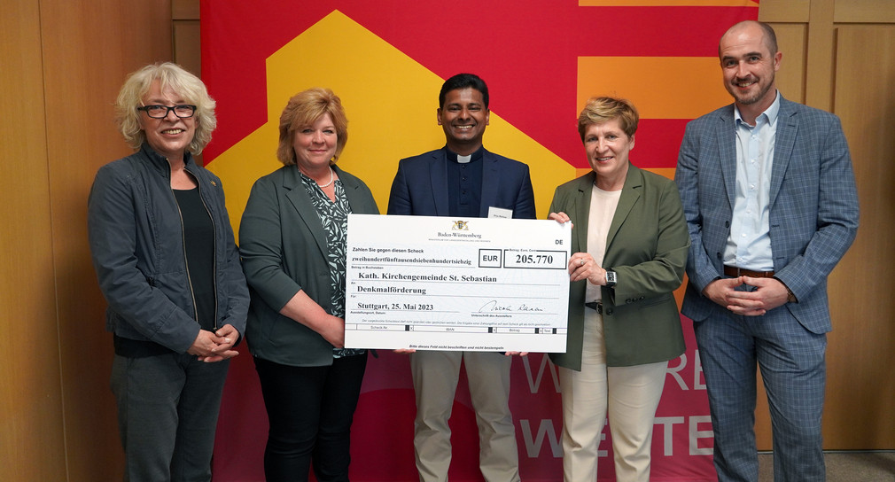 Symbolische Scheckübergabe im Rahmen der Denkmalförderung an die Katholische Kirchengemeinde St. Sebastian; von links: Martina Häusler MdL; Susanne Röhrle; Pfarrer Shiju Mathew; Nicole Razavi MdL, Ministerin für Landesentwicklung und Wohnen; Tim Bückner MdL