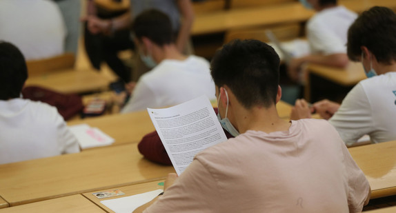 Studierende mit Mund-Nase-Schutz sitzen während einer Vorlesung in einem Hörsaal.