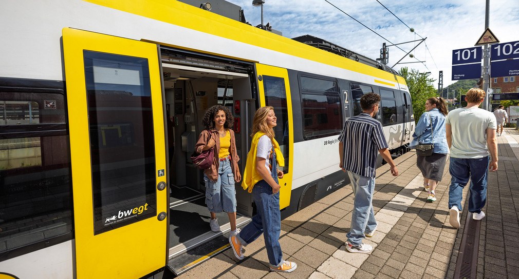 Junge Menschen steigen aus einem Zug am Bahnsteig aus.