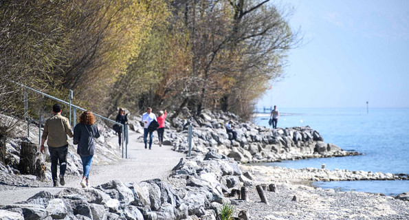 Menschen gehen auf einem Uferweg am Bodensee spazieren.