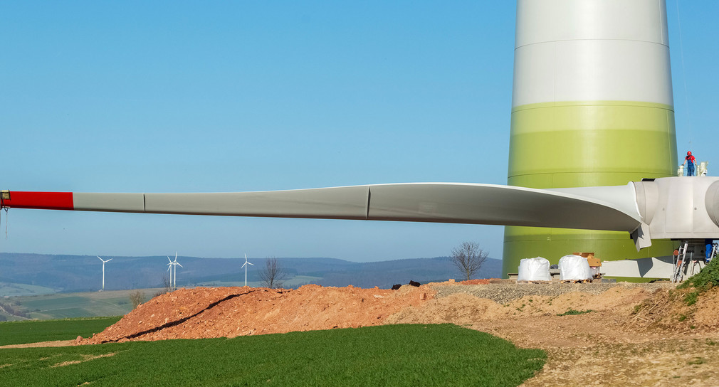 Auf einer Baustelle liegt ein vormontierter Rotor einer Windkraftanlage. Arbeiter bereiten den Rotor für die Montage am Windrad vor.