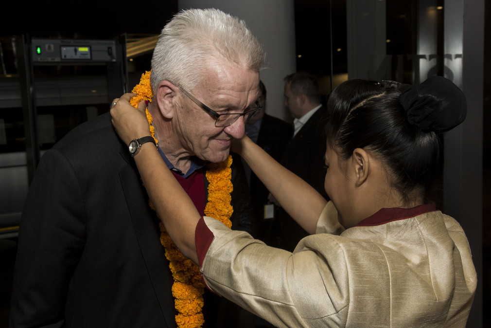 Eine Frau hängt Ministerpräsident Winfried Kretschmann zur Begrüßung in einem Hotel in Pune eine Kette um.