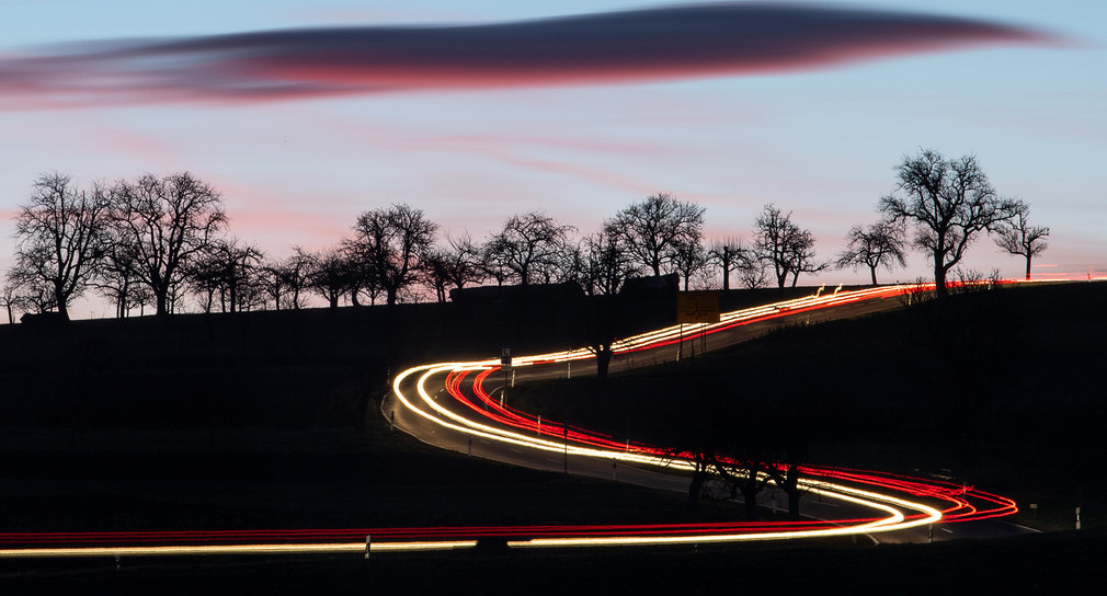 Autos fahren am frühen Morgen auf einer Landstraße bei Vaihingen an der Enz und hinterlassen eine Leuchtspur auf dem Foto.